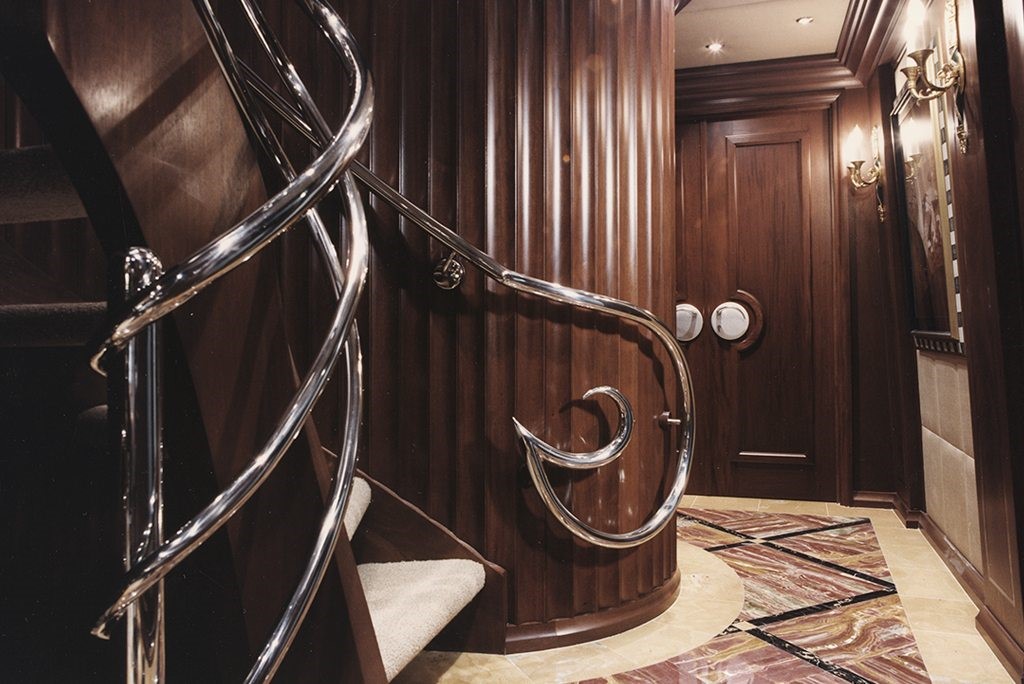 luxury yacht with mahogany stairwell with red marble-esque floor and silver fishhook shaped handrails