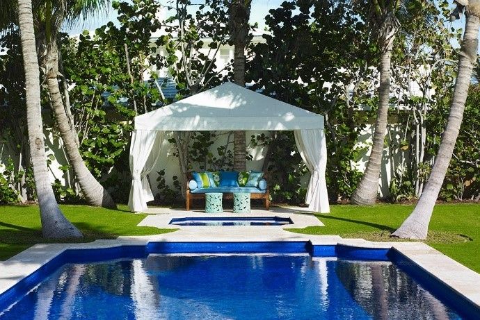 Traditionally designed pool in front of a small cabana with palm trees around it.