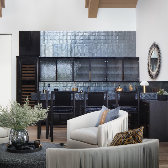 Fringed leather club chairs from Bradley lend a supple elegance to the club room’s sitting area. A sleek wet bar makes a dynamic statement with Silver Wave quartz countertops and polished Geoluxe surfaces. Lacquered cabinetry accented with metal framing adds a rich, glossy finish. #floridadesign #featured #pinecreek #modernranch #ranchdesign #clubroom