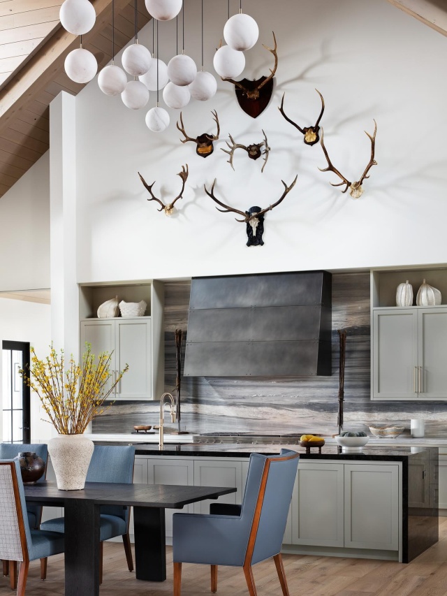 Soaring 25-foot vaulted ceilings set the stage for bold, sculptural statements in this kitchen. An orbed alabaster pendant from Schwung Home commands attention overhead, while a curated collection of antique deer antlers creates a radial focal point above a custom blackened-steel range hood. #ranchlife #kitchendesign #modernranch #ranchdesign #pinecreek #sportingclub #luxuryhomes #interiordesign #modernrustic